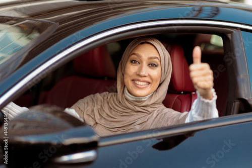 Great Car, I Like It. Portrait Of Smiling Muslim Woman In Hijab Gesturing Thumbs Up Sitting In Driver's Seat After Test Drive. Happy excited Arabian lady got driving license, gesturing okay sign