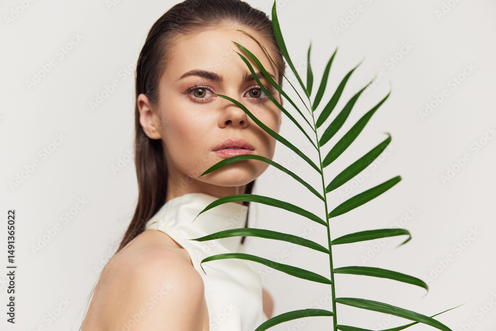 Naklejka premium Elegant young woman with fern in minimalist fashion portrait showcasing natural beauty and tranquility.