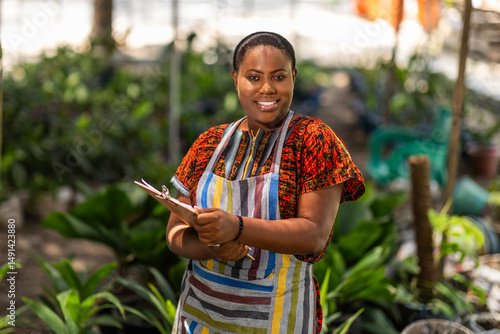 Konstfotografi Portrait of successful African woman small business owner into horticulture standing in her garden surrounded by green potted plants