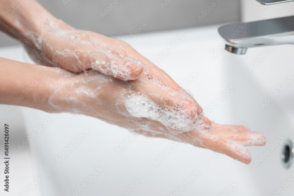 Woman washing hands at sink in bathroom, closeup Woman washing hands at sink in bathroom, closeup