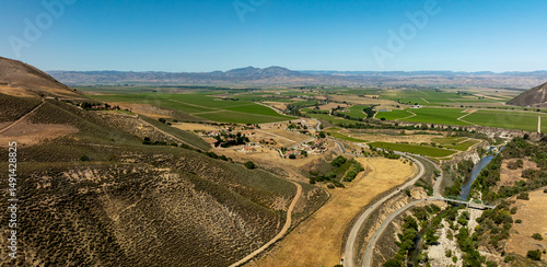 Afternoon sunlight touches spring vineyards in a panoramic landscape of rolling hills and distant mountains under a vast sky.  Aerial view of Greenfield from Arroyo Seco