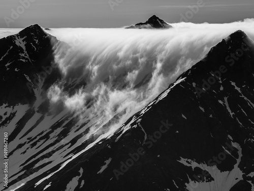 Dramatic black and white landscape of a cloud waterfall cascading over mountain peaks near Hornsund, Svalbard
