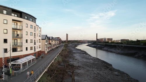  Row of apartment houses on waterfront. Backwards revealing of low water in riverbed and footbridge over. Newport, Wales, UK