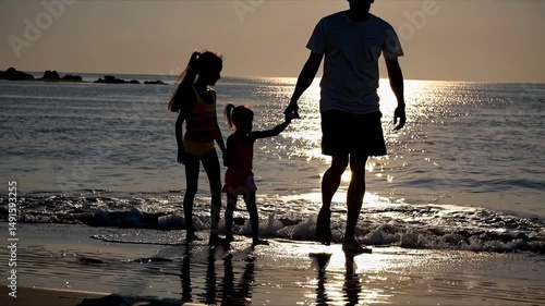Silhouette of a family walking on the beach at sunset, captured from a low angle. The video conveys warmth and togetherness in a serene setting.