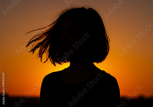 Silhouette of a young girl with windswept hair against a vibrant sunset sky capturing youthful innocence and natural beauty