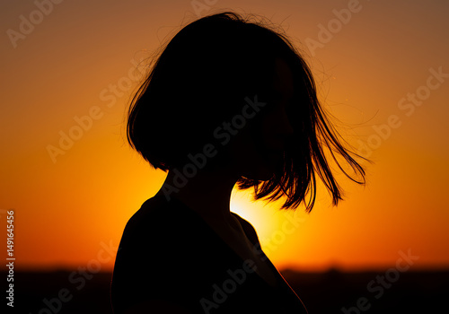 Silhouetted woman with short hair enjoying a vibrant sunset scene