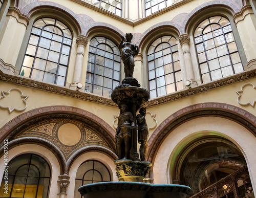 Canvas Print Vienna – View of the Ferstel Passage fountain, the elegant Renaissance Revival bronze sculpture surrounded by the arcade's ornate ironwork and glass-domed ceiling, creating a jewel-like centerpiece
