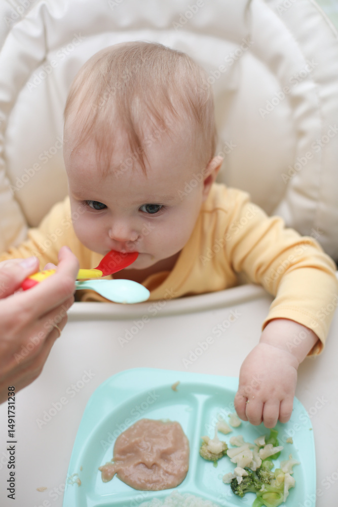 Cute little baby eats food from a plate at a table Cute little baby eats food from a plate at a table