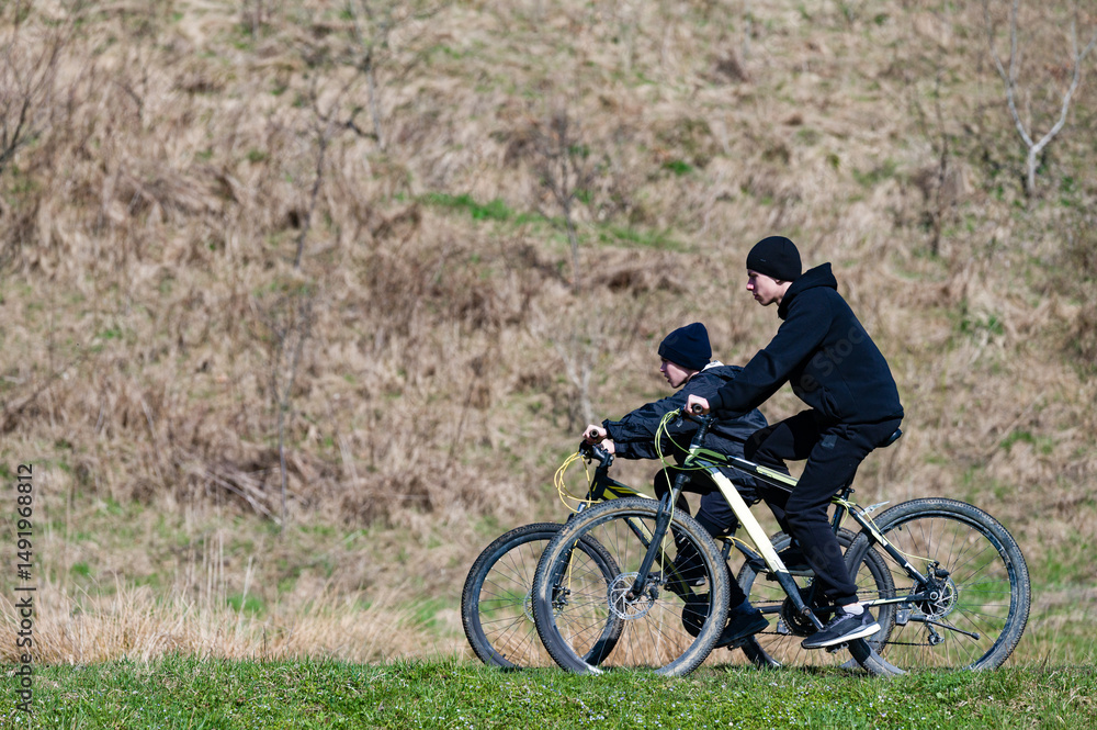 Fototapeta premium Two people biking together on a grassy hill, enjoying a sunny day outdoors.