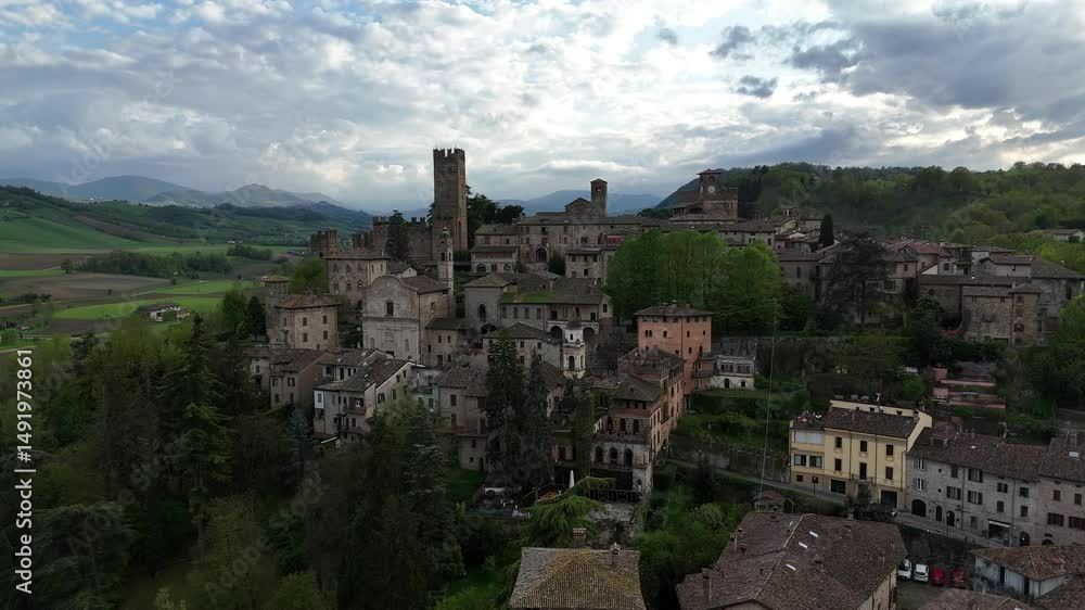 Drone view of Castell'Arquato medieval skyline showing Visconti Castle, clock tower and stone houses, surrounded by hills and woods, overcast spring sky Drone view of Castell'Arquato medieval skyline showing Visconti Castle, clock tower and stone houses, surrounded by hills and woods, overcast spring sky