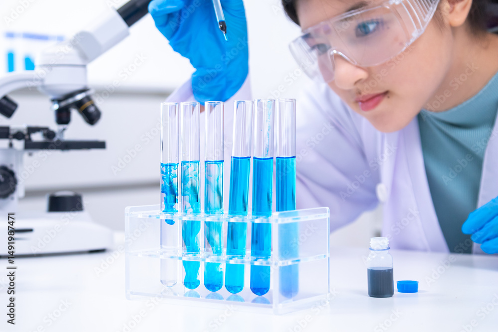 Fototapeta premium Teen scientist girl conducting science test by carefully evaluating blue solution in laboratory. Science, laboratory, experiment, and research demonstrate academic progress and practical skills.
