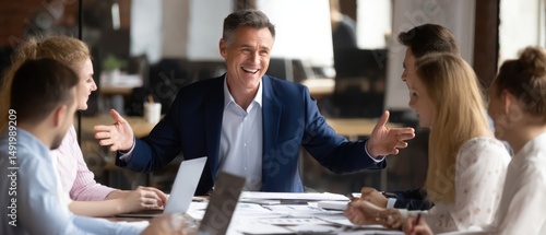 A business meeting with a smiling leader engaging a team, surrounded by laptops and documents in a modern office setting.