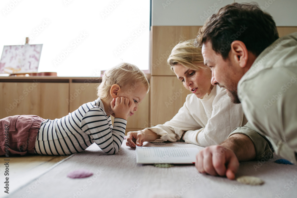 Fototapeta premium Parents reading book with little son, sitting on floor.