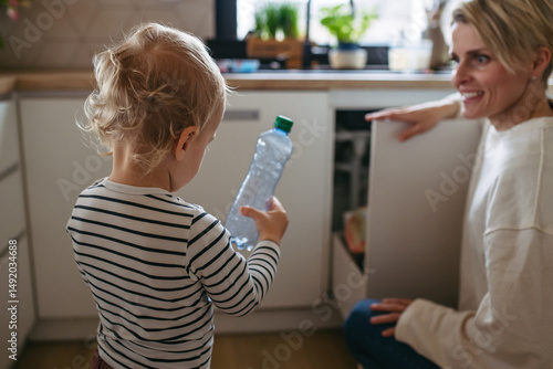 Fotografie Mother teaching toddler to sort waste into recycling bin.