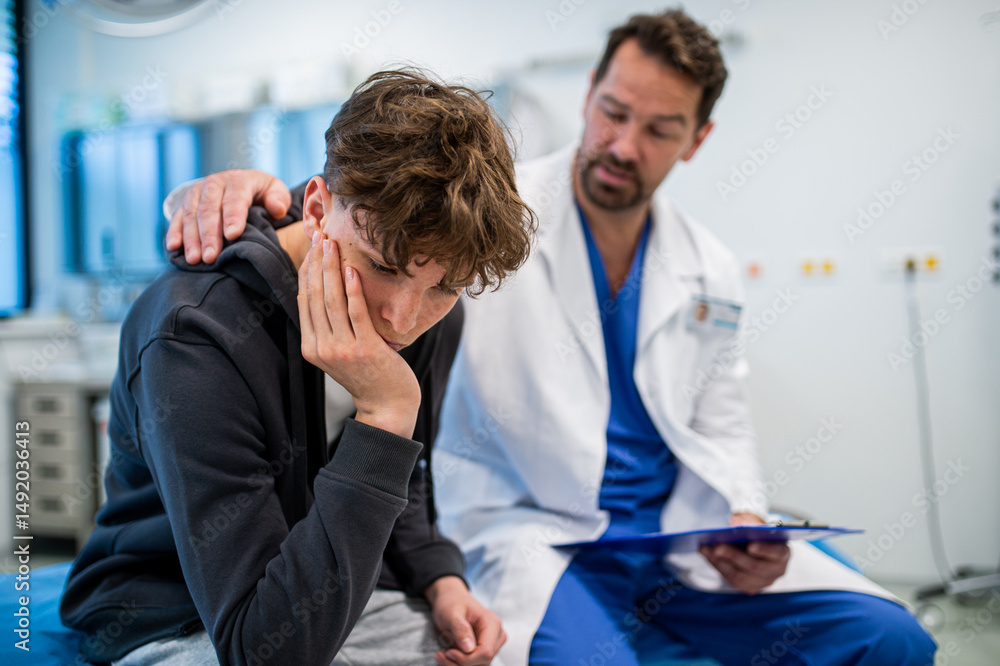 Fototapeta premium Depressed teenage patient sitting on hospital bed, talking with caring doctor.