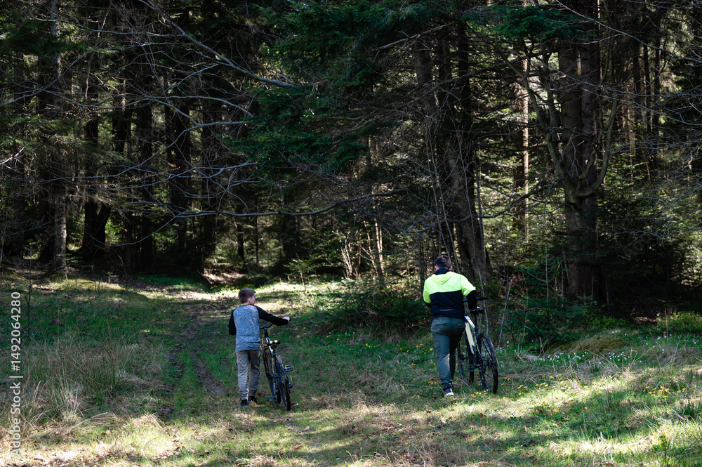 Fototapeta premium Father and son walk bikes through forest trail