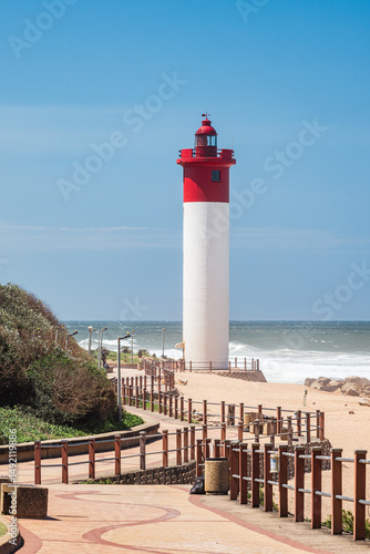 Fototapeta A striking red and white lighthouse stands tall on a sunny day along the Umhlanga beachfront promenade in KwaZulu-Natal, South Africa