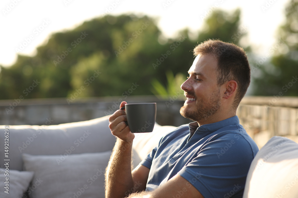 Happy man drinking coffee sitting in an exterior sofa Happy man drinking coffee sitting in an exterior sofa