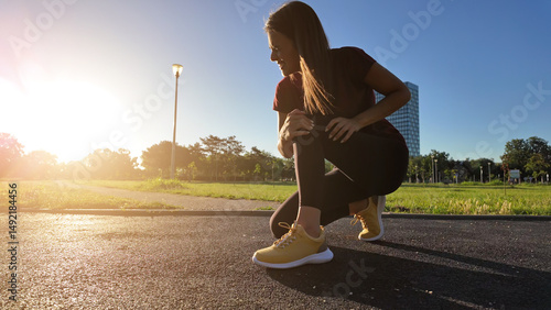 Фотография Young woman with knee and leg pain during jogging and exercise in urban park