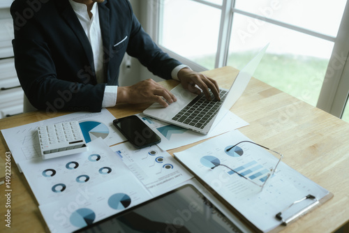 Photos A businesswoman sits at a desk in a corporate office, analyzing financial documents, charts, and reports while discussing strategy and growth