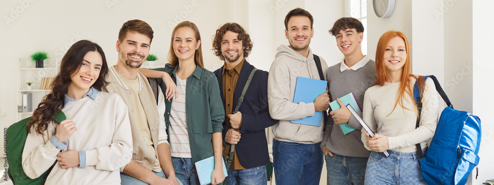 Fototapeta premium Happy university students with notebooks and backpacks standing next to each other in row in room, being friendly groupmates, satisfied after successfully passed exams. Education concept