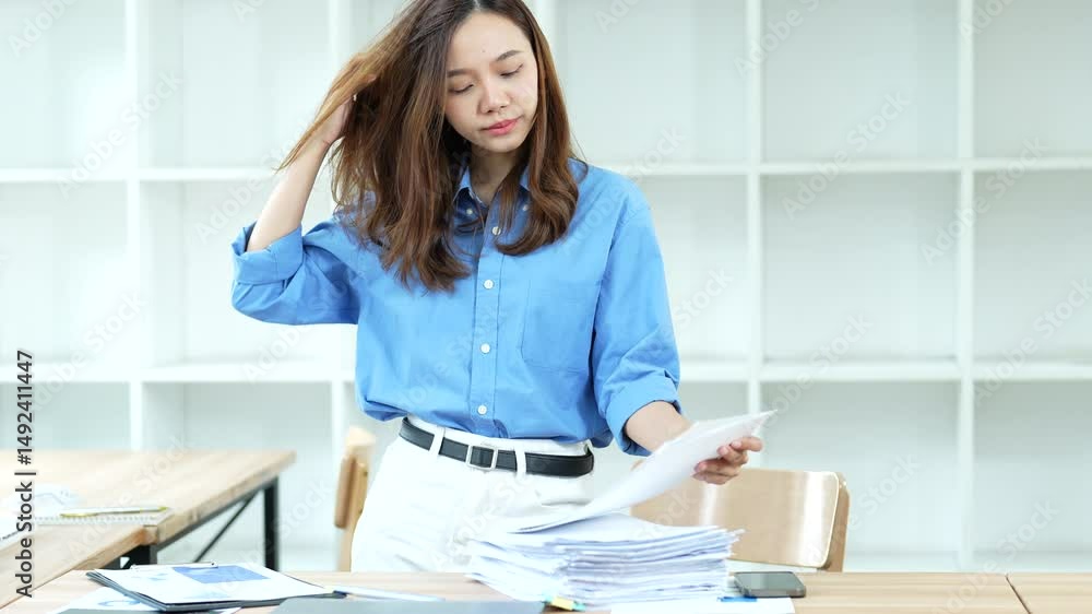 Stressed businesswoman experiencing work pressure, examining paperwork and holding folder while touching head, signaling professional challenges in corporate environment Stressed businesswoman experiencing work pressure, examining paperwork and holding folder while touching head, signaling professional challenges in corporate environment