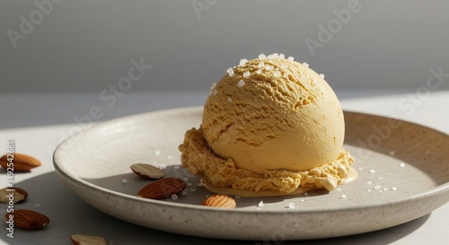 Creamy golden ice cream scoop on a textured plate garnished with sea salt and surrounded by fresh nuts, perfect for food enthusiasts and dessert lovers