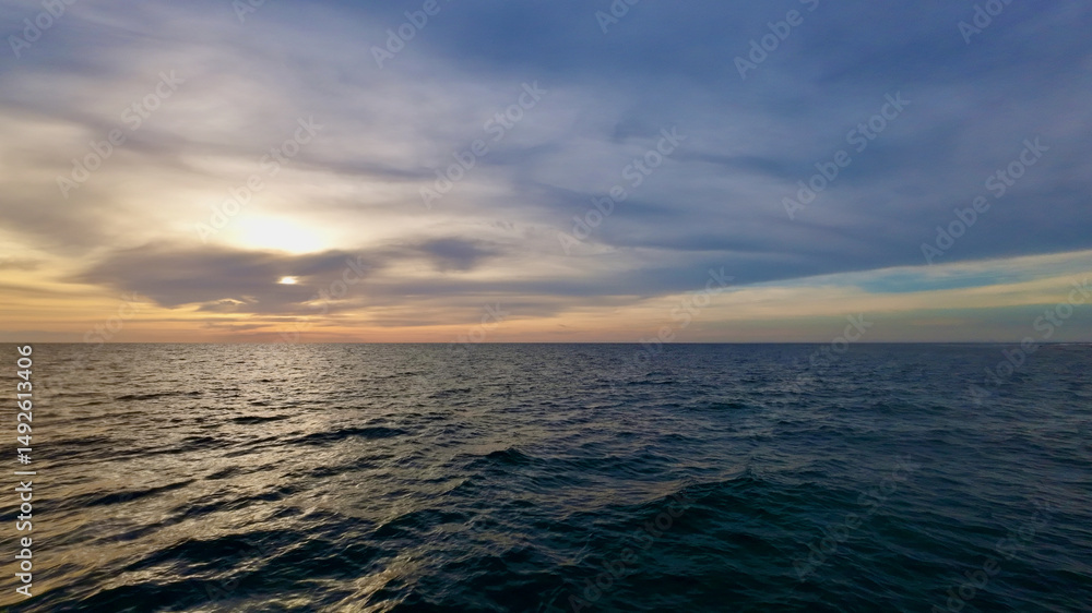 Fototapeta premium Picturesque sunset over the sea. View of the calm surface of the sea and clouds above the horizon during sunset.
