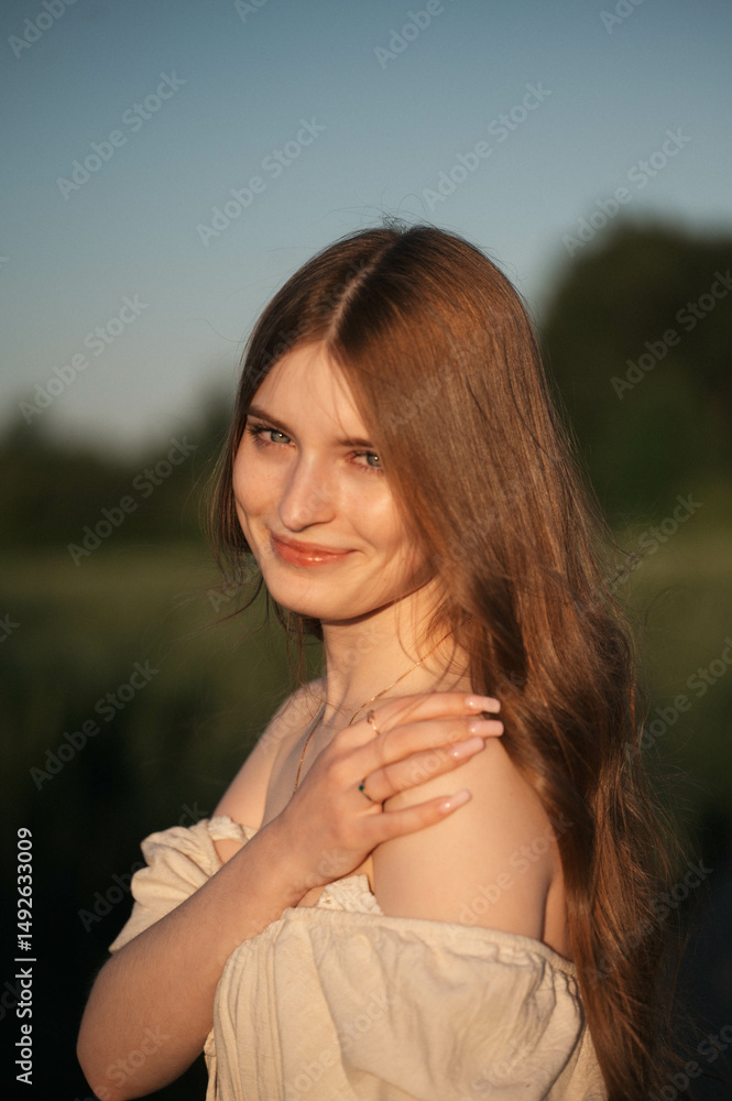 Fototapeta premium Elegant woman with long dark hair wearing a beige dress in a rural field at sunset, emotional close-up with warm backlight and soft tones, natural beauty in outdoor setting
