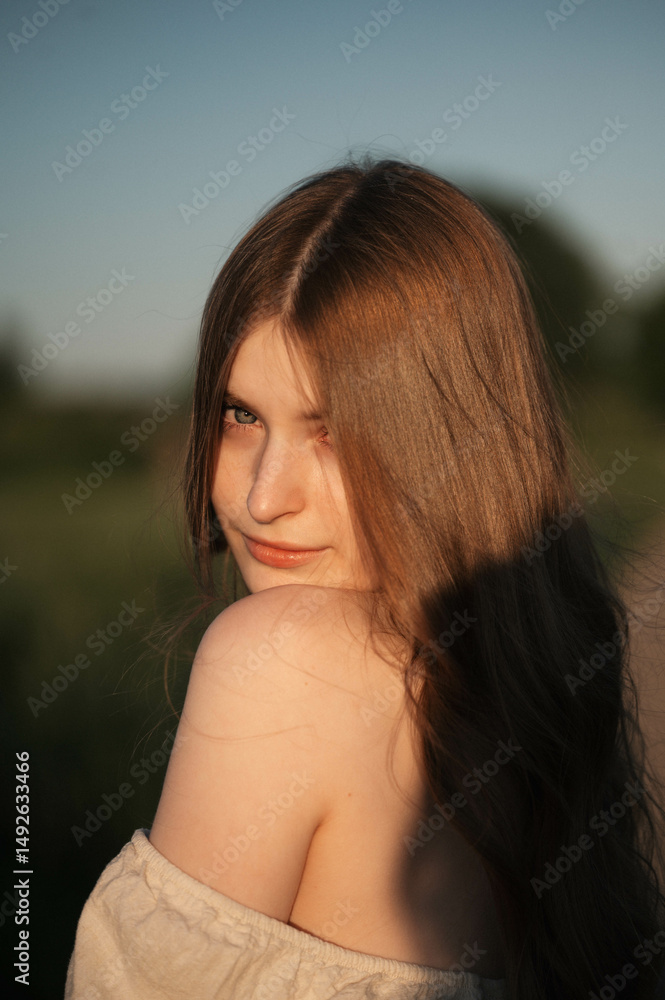 Naklejka premium Elegant woman with long dark hair wearing a beige dress in a rural field at sunset, emotional close-up with warm backlight and soft tones, natural beauty in outdoor setting