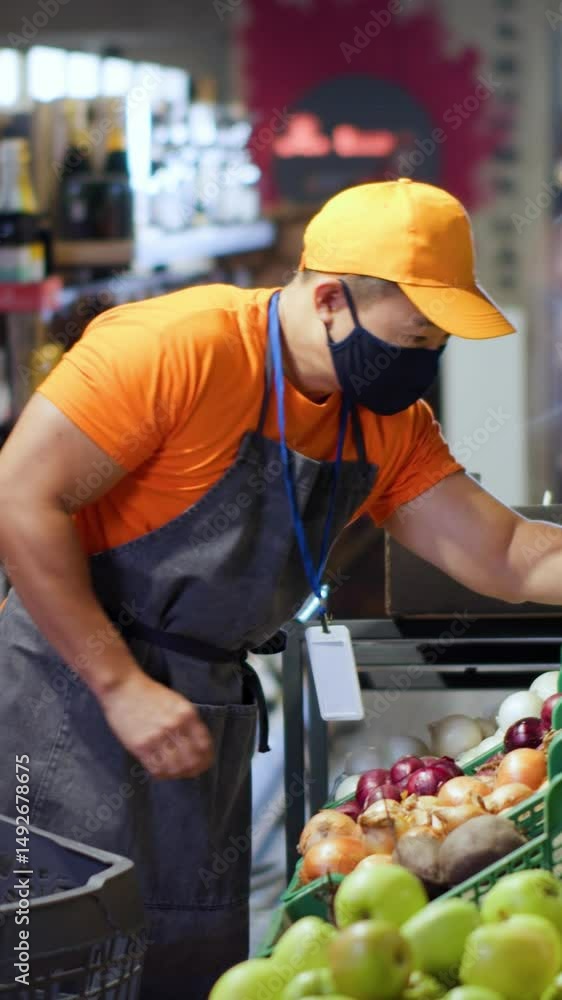 Asian busy shop assistant arranging foods on shelves collecting lettuce in grocery store. Chinese seller guy with face mask using tablet computer at organic supermarket. Asian busy shop assistant arranging foods on shelves collecting lettuce in grocery store. Chinese seller guy with face mask using tablet computer at organic supermarket.
