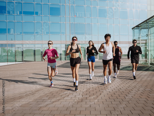 Φωτογραφία Seven young athletes run outdoors in front of a modern glass building
