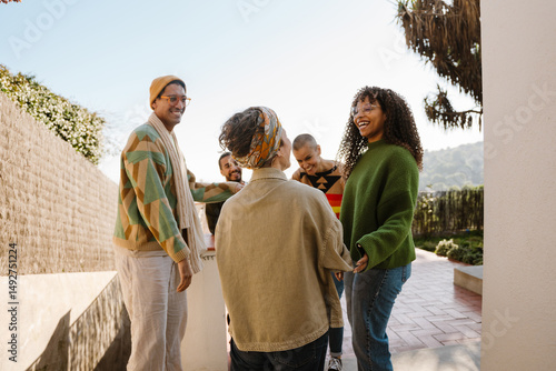 Slika na platnu A group of multiracial adult men and women stand outdoors in casual clothing, smiling and talking in a sunny urban setting