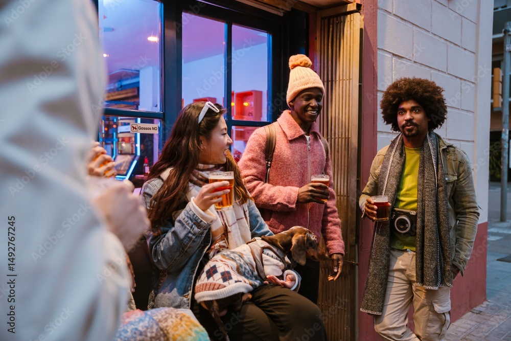 Obraz premium Several friends stand outside a bar, sipping beers and chatting while one woman holds a small dog in a sweater. The concept of evening meeting with friends in a city.