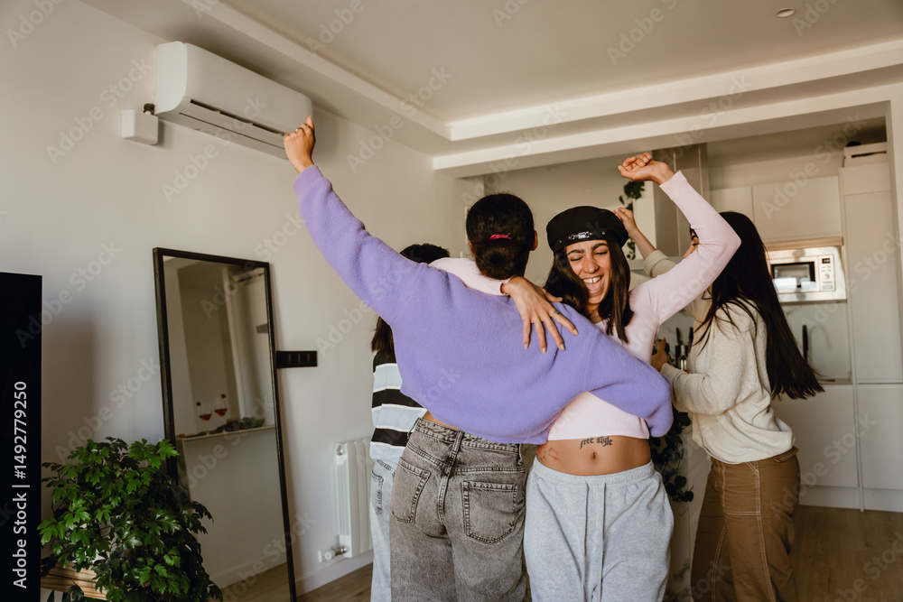 Obraz premium A multinational group of young women is dancing at a girls' party in a cozy apartment, wearing comfortable home outfits, laughing together near the kitchen, and enjoying a carefree indoor celebration.