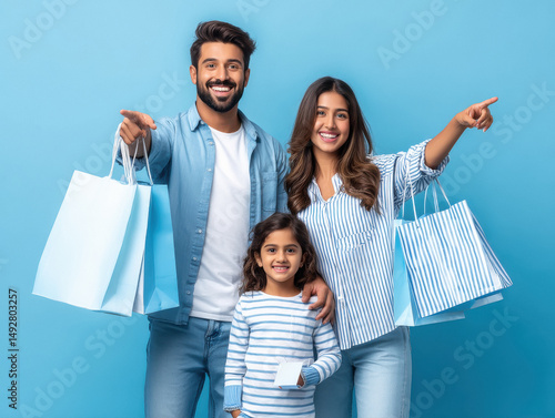 a modern indian family of three standing together against a solid bright blue background.