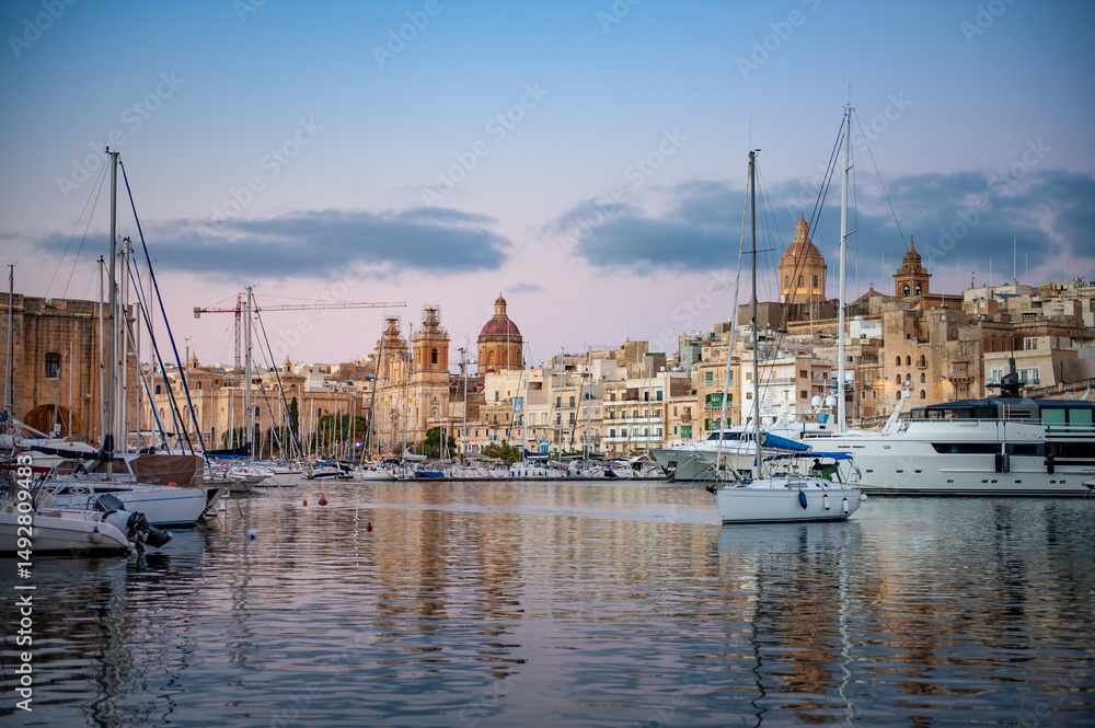 Spectacular view of the moored sailing yachts in seaport Vittoriosa and St. Lawrence's Catholic Church. Location place Birgu harbour, Malta, Europe. Photo wallpapers. Golden hour. Spectacular view of the moored sailing yachts in seaport Vittoriosa and St. Lawrence's Catholic Church. Location place Birgu harbour, Malta, Europe. Photo wallpapers. Golden hour.