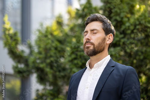 Wallpaper Mural A well-dressed man with eyes closed enjoys a moment of peace outdoors, surrounded by greenery, looking calm and serene. Torontodigital.ca