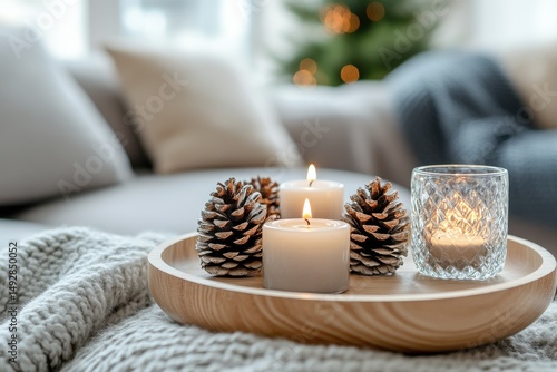Cozy Winter Atmosphere with Candles, Pinecones, and Decorative Elements on a Light Gray Knit Blanket Beside a Sofa and Soft Christmas Tree Bokeh Background