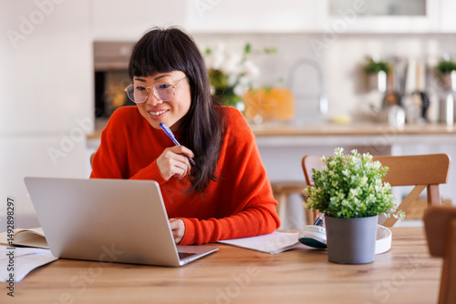Woman taking notes in planner while having online meeting