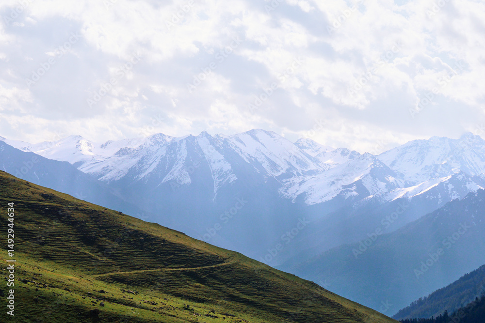 Fototapeta premium a mountain road on a slope with a view of the snowy peaks. Morning in the mountains