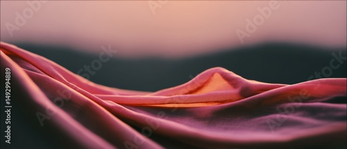 Draped pink fabric rolls smoothly over a landscape, kissed by soft sunset light, exuding warmth and allure.