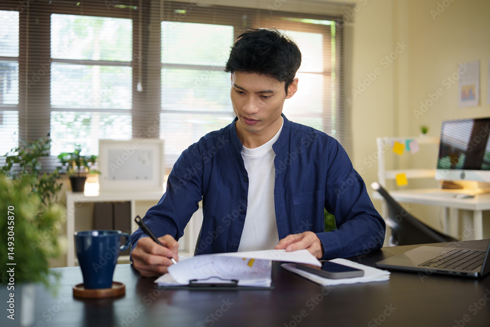 Focused businessman reviewing paperwork while working at a modern office desk. Focused businessman reviewing paperwork while working at a modern office desk.
