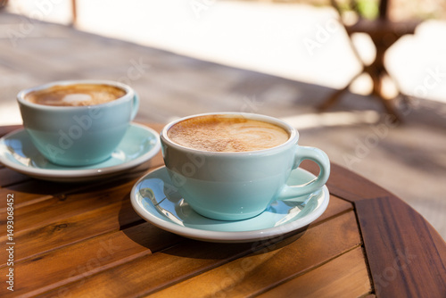Café cappuccino mousseux en terrasse sur une table en bois au soleil servi dans des tasses bleues