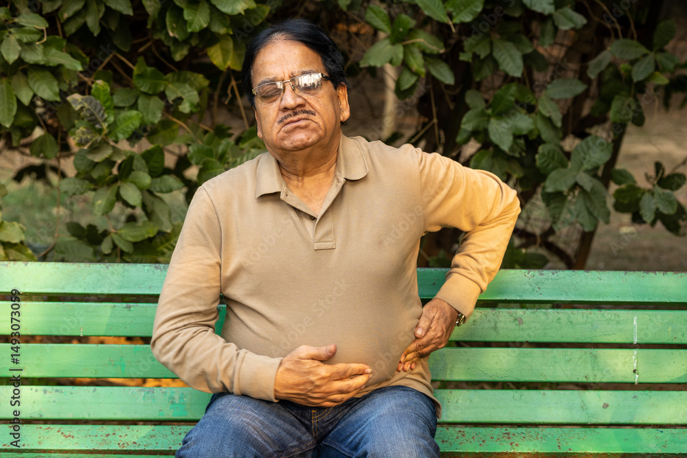 Obraz premium Indian painful senior man suddenly suffering stomach pain at park