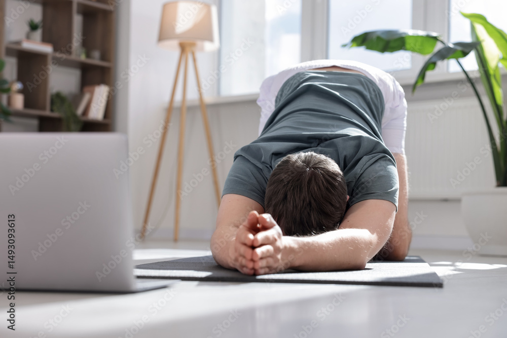 Fototapeta premium Man having online yoga class via laptop at home