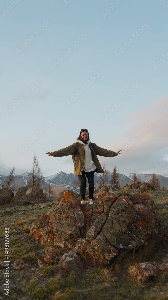 A young girl tourist with a backpack on her shoulders runs to the top of the mountain, climbs a rock and enjoys the panoramic view at sunset. Vertical video. A young girl tourist with a backpack on her shoulders runs to the top of the mountain, climbs a rock and enjoys the panoramic view at sunset. Vertical video.
