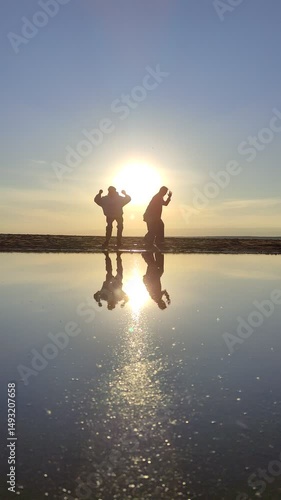 Happy family at sunset on the sea.
Silhouettes of people dancing on the shore and reflected in the water.