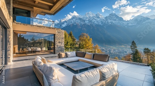 Modern luxury patio with mountain views.  A spacious outdoor living area features comfortable seating,  a sleek coffee table, and panoramic vistas of snow-capped peaks