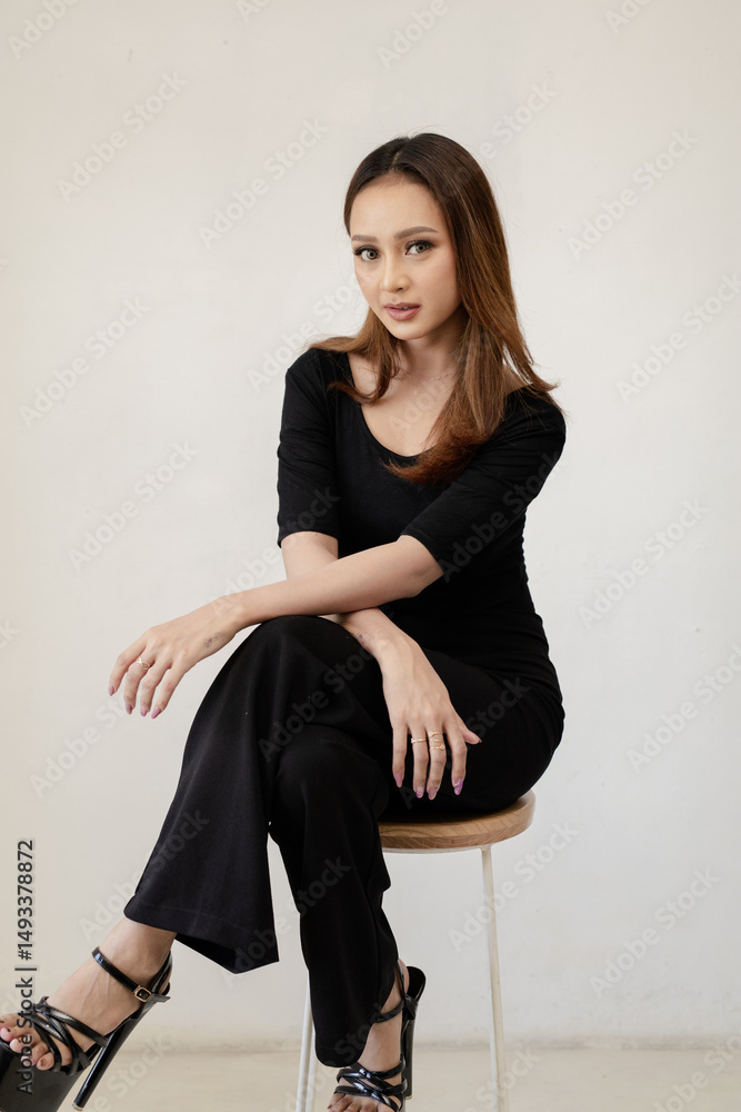 Attractive woman in black outfit poses confidently while seated on a stool indoors Attractive woman in black outfit poses confidently while seated on a stool indoors
